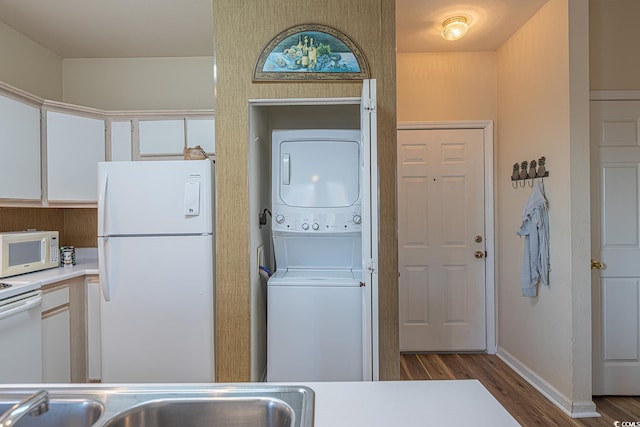 laundry area with stacked washer / drying machine, laundry area, wood finished floors, a sink, and baseboards