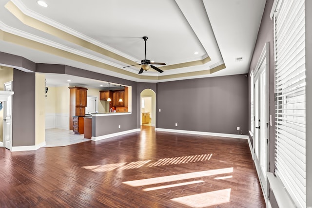 unfurnished living room with a raised ceiling, crown molding, ceiling fan, and dark wood-type flooring