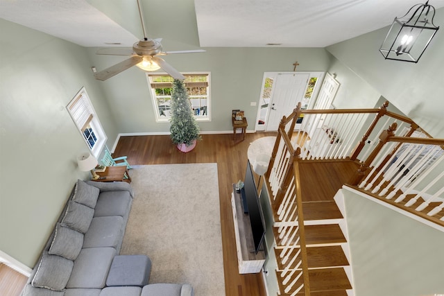 stairway with ceiling fan with notable chandelier, hardwood / wood-style flooring, and vaulted ceiling