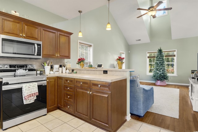 kitchen featuring kitchen peninsula, appliances with stainless steel finishes, pendant lighting, light hardwood / wood-style flooring, and high vaulted ceiling