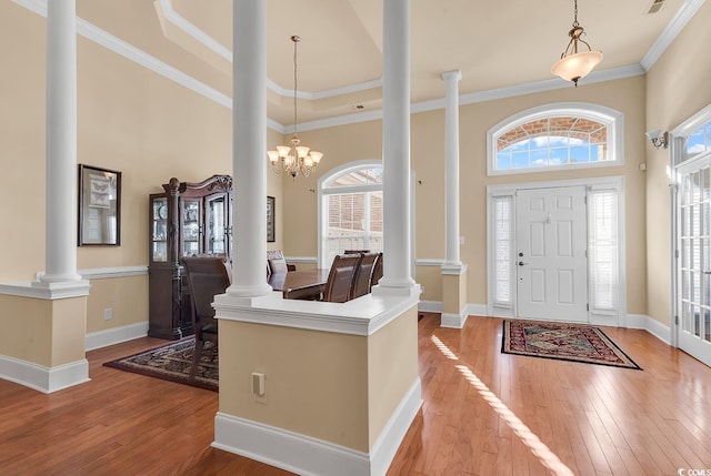 foyer with an inviting chandelier, light hardwood / wood-style flooring, decorative columns, crown molding, and a towering ceiling