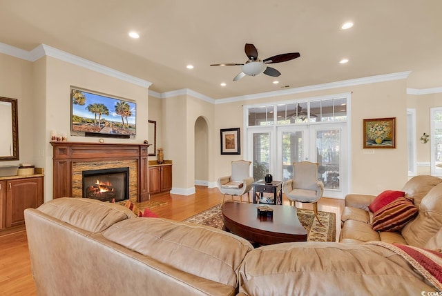 living room featuring ceiling fan, light hardwood / wood-style floors, a stone fireplace, and crown molding