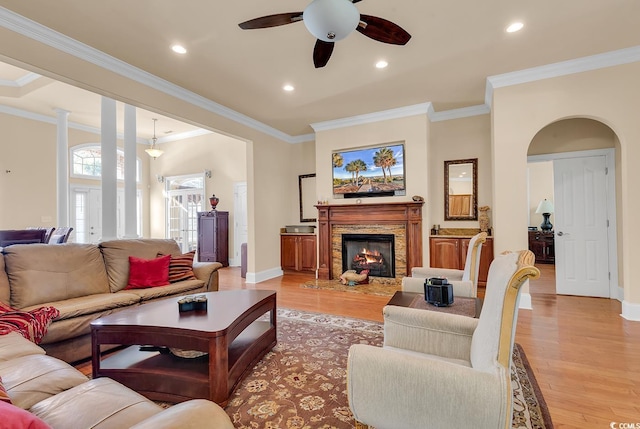 living room with ceiling fan, ornamental molding, a fireplace, and light hardwood / wood-style flooring