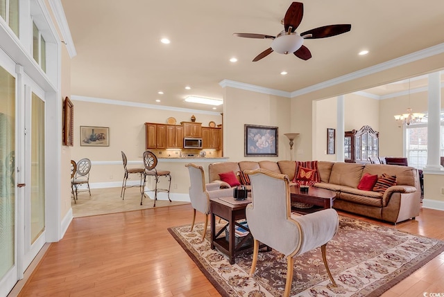 living room with ceiling fan with notable chandelier, light hardwood / wood-style flooring, and crown molding