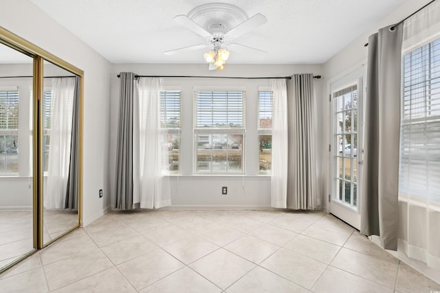 unfurnished dining area featuring ceiling fan, a healthy amount of sunlight, light tile patterned floors, and a textured ceiling