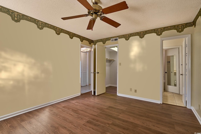 unfurnished bedroom with a walk in closet, a textured ceiling, ceiling fan, wood-type flooring, and a closet