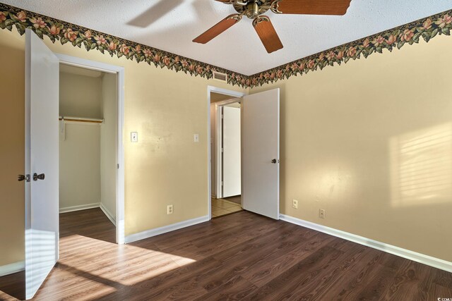 unfurnished bedroom featuring dark hardwood / wood-style floors, ceiling fan, a walk in closet, and a textured ceiling