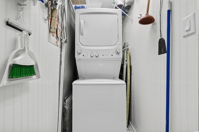 washroom featuring stacked washer / drying machine and wooden walls