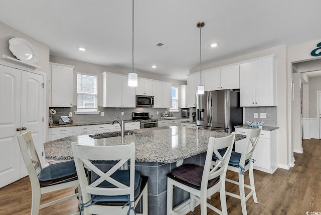 kitchen with stainless steel appliances, hanging light fixtures, a center island with sink, and sink