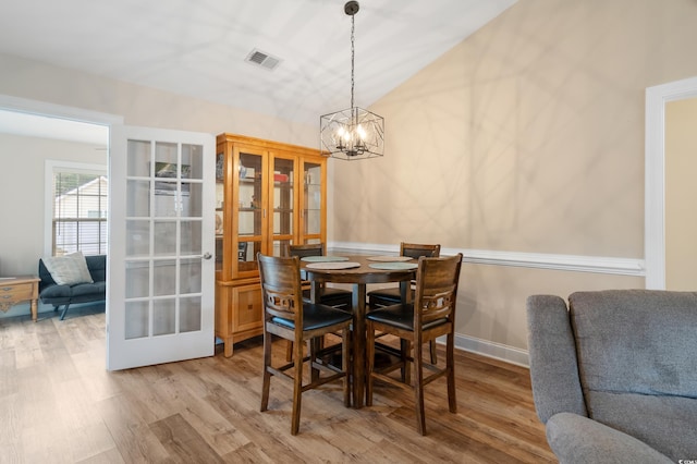 dining area with an inviting chandelier, vaulted ceiling, and light wood-type flooring