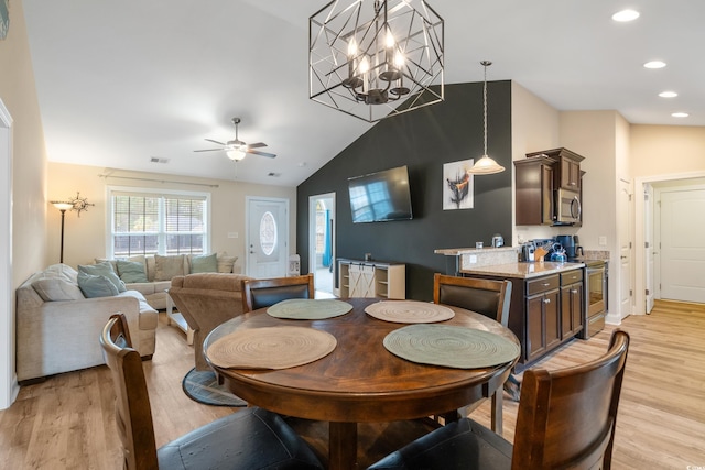 dining room with light hardwood / wood-style flooring, ceiling fan with notable chandelier, and vaulted ceiling