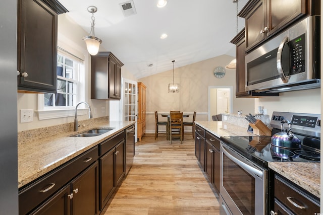 kitchen with appliances with stainless steel finishes, vaulted ceiling, sink, pendant lighting, and light hardwood / wood-style floors