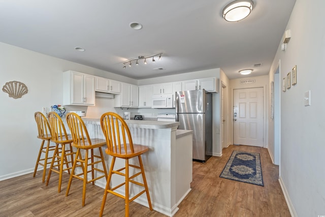 kitchen featuring a breakfast bar, white appliances, white cabinets, light hardwood / wood-style floors, and kitchen peninsula