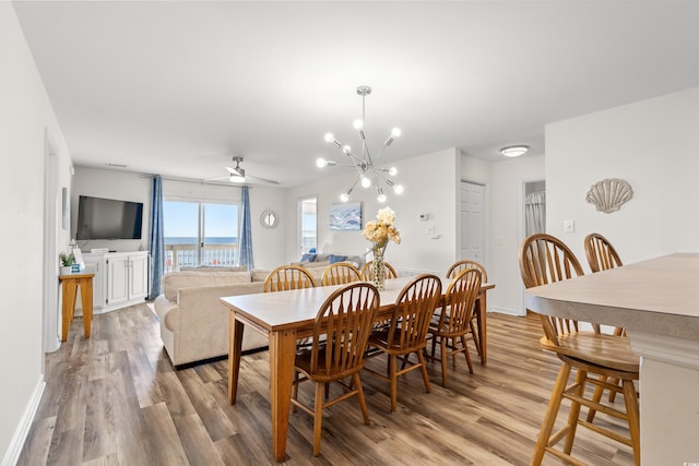 dining room with ceiling fan with notable chandelier and light wood-type flooring