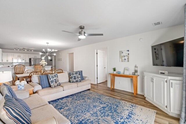 living room featuring ceiling fan with notable chandelier and light wood-type flooring