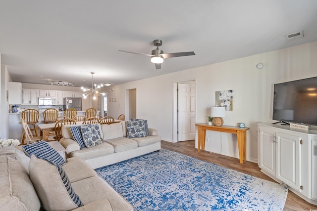 living room featuring ceiling fan with notable chandelier and light hardwood / wood-style floors