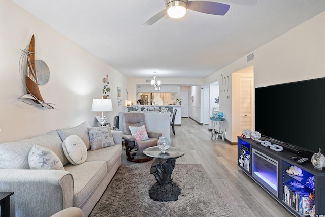 living room with ceiling fan with notable chandelier and light hardwood / wood-style flooring