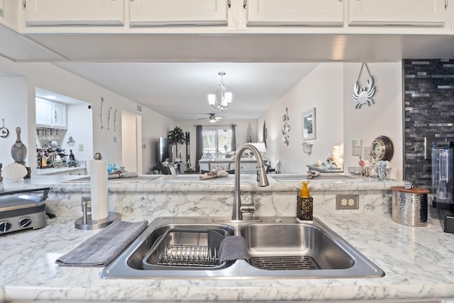 kitchen featuring white cabinets, a notable chandelier, light stone countertops, and sink