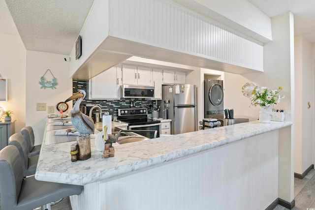 kitchen with white cabinetry, stainless steel appliances, light hardwood / wood-style flooring, kitchen peninsula, and decorative backsplash