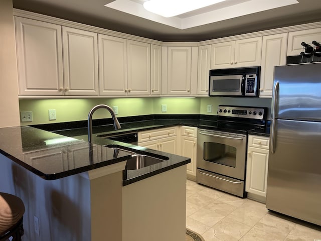 kitchen featuring white cabinets, kitchen peninsula, stainless steel appliances, and dark stone counters