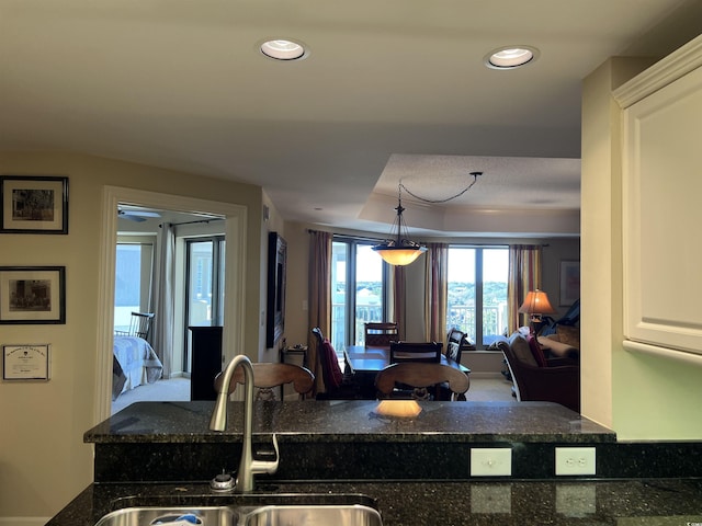 kitchen featuring white cabinetry, sink, hanging light fixtures, and dark stone counters