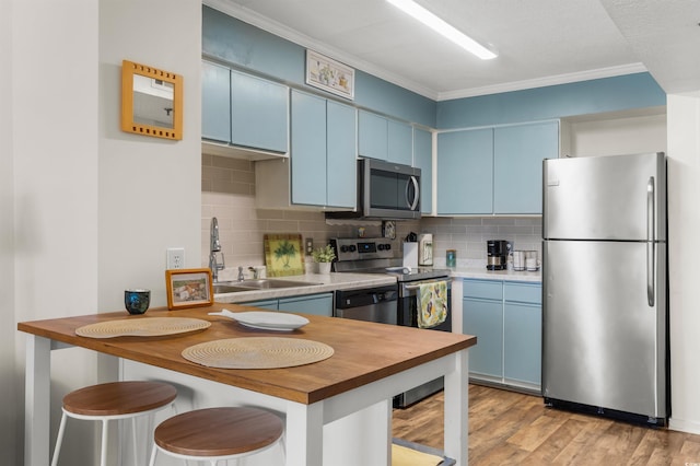 kitchen featuring blue cabinetry, light wood-type flooring, stainless steel appliances, and crown molding