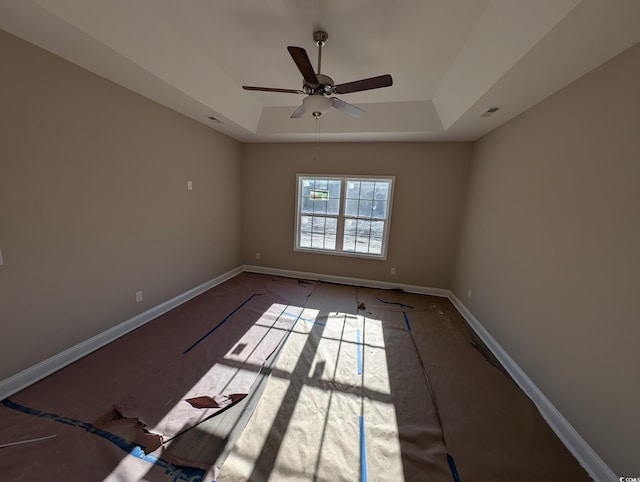 empty room with ceiling fan and a tray ceiling