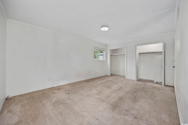 unfurnished bedroom featuring light carpet, multiple closets, and crown molding