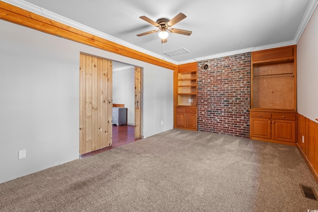 interior space featuring ornamental molding, brick wall, ceiling fan, wooden walls, and carpet floors