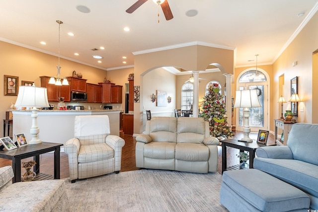 living room with ceiling fan with notable chandelier, light wood-type flooring, ornate columns, and ornamental molding