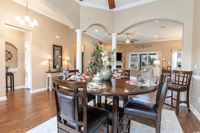 dining space featuring ceiling fan with notable chandelier, crown molding, a towering ceiling, dark hardwood / wood-style flooring, and decorative columns