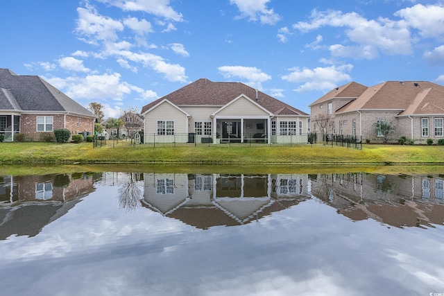 rear view of property featuring a lawn, a sunroom, and a water view