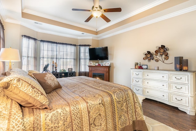 bedroom with a tray ceiling, dark hardwood / wood-style flooring, ceiling fan, and crown molding