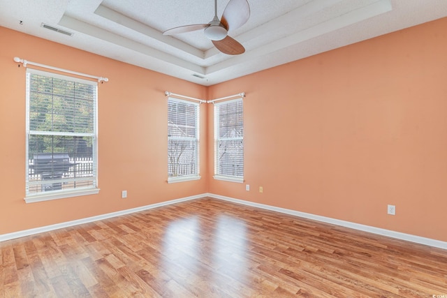 unfurnished room with a tray ceiling, ceiling fan, light hardwood / wood-style flooring, and a textured ceiling