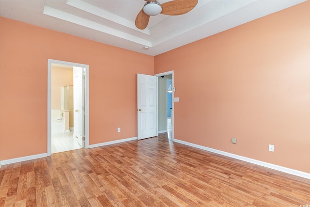 unfurnished bedroom featuring a raised ceiling, ensuite bathroom, ceiling fan, and light hardwood / wood-style floors