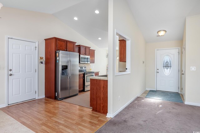 kitchen with lofted ceiling, decorative backsplash, appliances with stainless steel finishes, and light hardwood / wood-style flooring