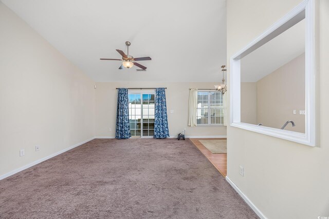 empty room with ceiling fan with notable chandelier, carpet, and vaulted ceiling