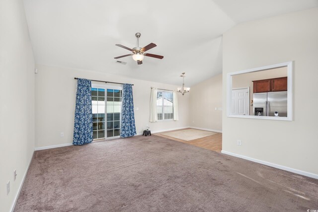 unfurnished living room featuring ceiling fan with notable chandelier, carpet flooring, and vaulted ceiling