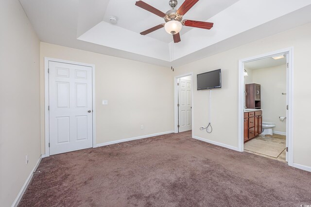 unfurnished bedroom featuring ceiling fan, light carpet, a tray ceiling, and connected bathroom