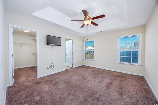 unfurnished bedroom featuring a spacious closet, ceiling fan, a raised ceiling, a closet, and carpet flooring