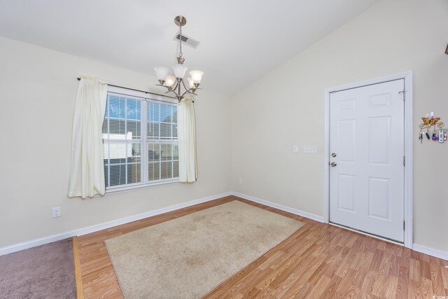 empty room with vaulted ceiling, a notable chandelier, and hardwood / wood-style floors