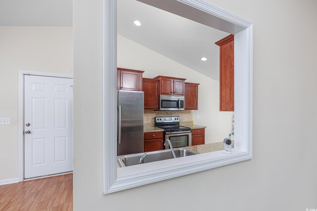 kitchen with backsplash, vaulted ceiling, sink, light hardwood / wood-style flooring, and appliances with stainless steel finishes