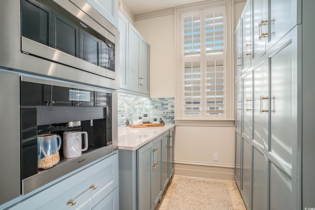 kitchen featuring gray cabinetry, light stone countertops, stainless steel appliances, tasteful backsplash, and crown molding