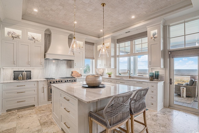 kitchen featuring stainless steel range, a kitchen island, white cabinets, a water view, and custom exhaust hood