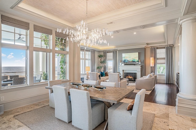 dining space featuring light wood-type flooring, ornate columns, a raised ceiling, crown molding, and a water view