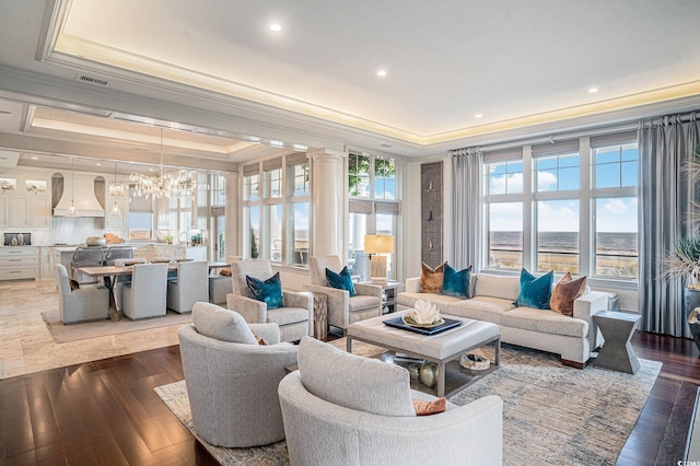 living room featuring hardwood / wood-style flooring, a water view, a tray ceiling, and a notable chandelier