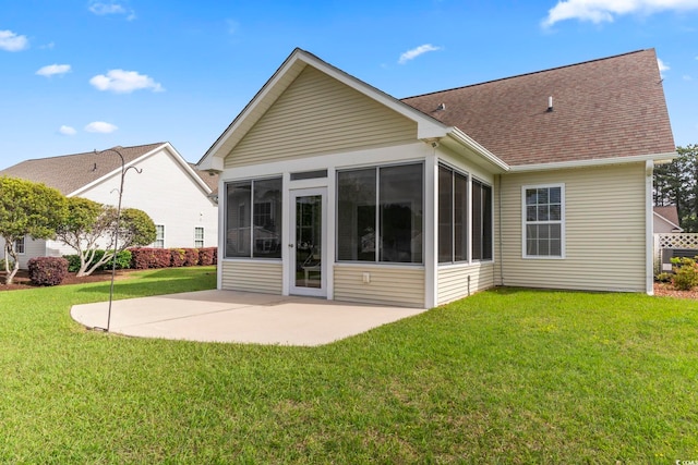 back of house featuring a sunroom, a patio area, a lawn, and a shingled roof