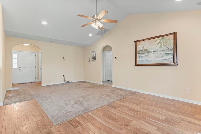 unfurnished living room featuring arched walkways, light wood finished floors, a ceiling fan, baseboards, and vaulted ceiling