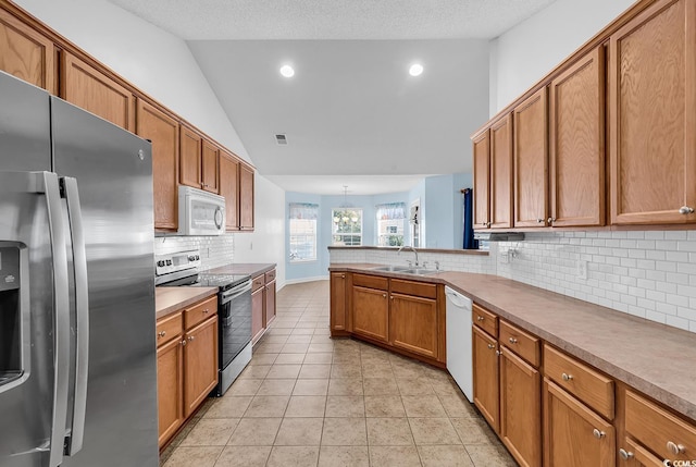 kitchen with lofted ceiling, sink, light tile patterned floors, appliances with stainless steel finishes, and kitchen peninsula