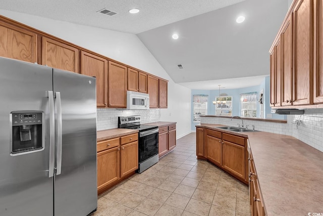 kitchen featuring sink, stainless steel appliances, pendant lighting, a textured ceiling, and vaulted ceiling